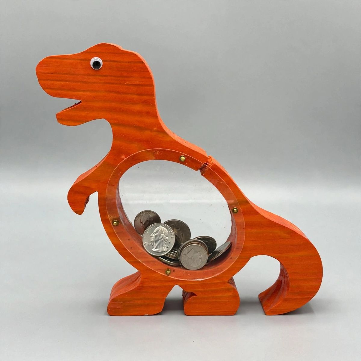 Orange-red wooden T Rex coin bank with coins visible through its clear belly window
